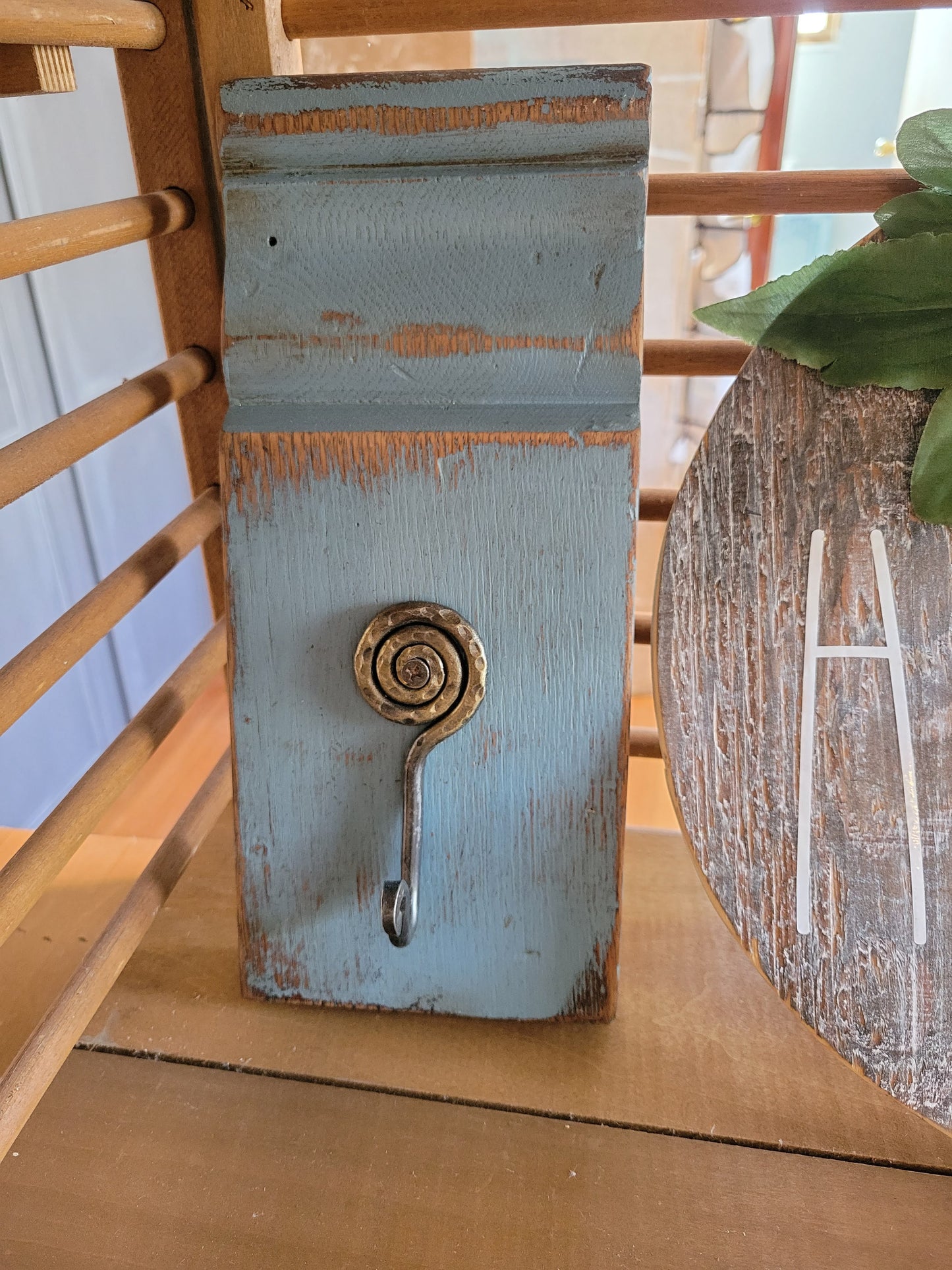 This gorgeous plinth was recovered from an old farm house. It has been painted blue and sanded. The interesting hammered metal spiral hook adds another dimension to this wall décor.