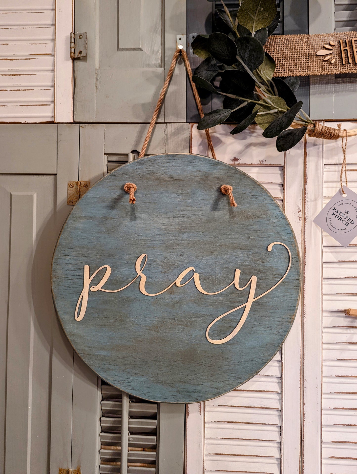 Round wooden sign painted teal with jute hanger and laser cut word "pray." Create this round sign door hanger! Paint or stain the wooden circle, paint your laser cut word, drill holes for the hanger.