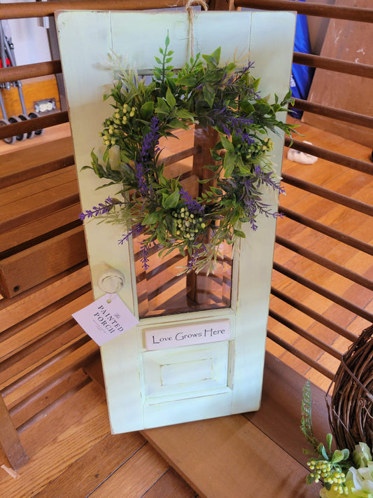 Small light green cabinet door sign with a lavender and greenery wreath and small handwritten sign "Love Grows Here."