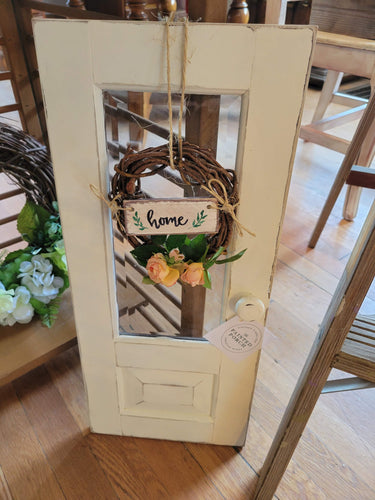 Small cabinet door with a pink rose wreath and small handwritten sign 