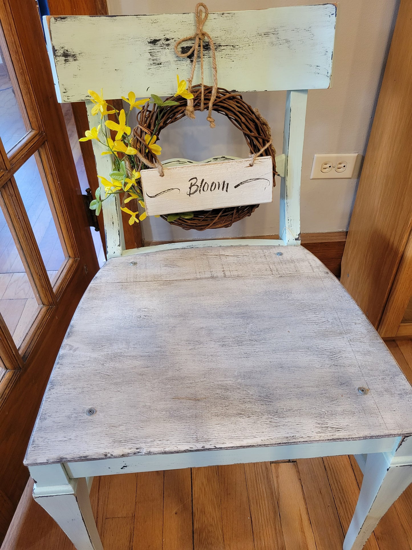 Mint green chair, flat seat to hold potted plants, forsythia wreath, small wooden "Bloom" sign