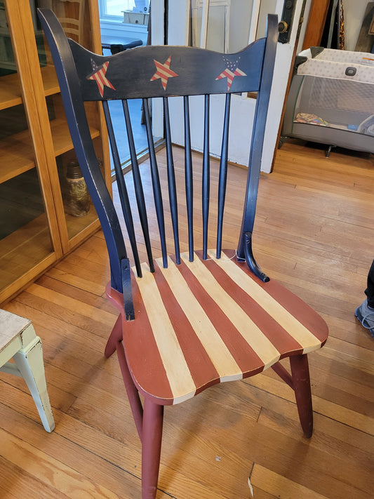 A vintage dining room chair that has been refinished in an Americana style. Fabric stars glued along the top of the chair and stripes painted on the seat.