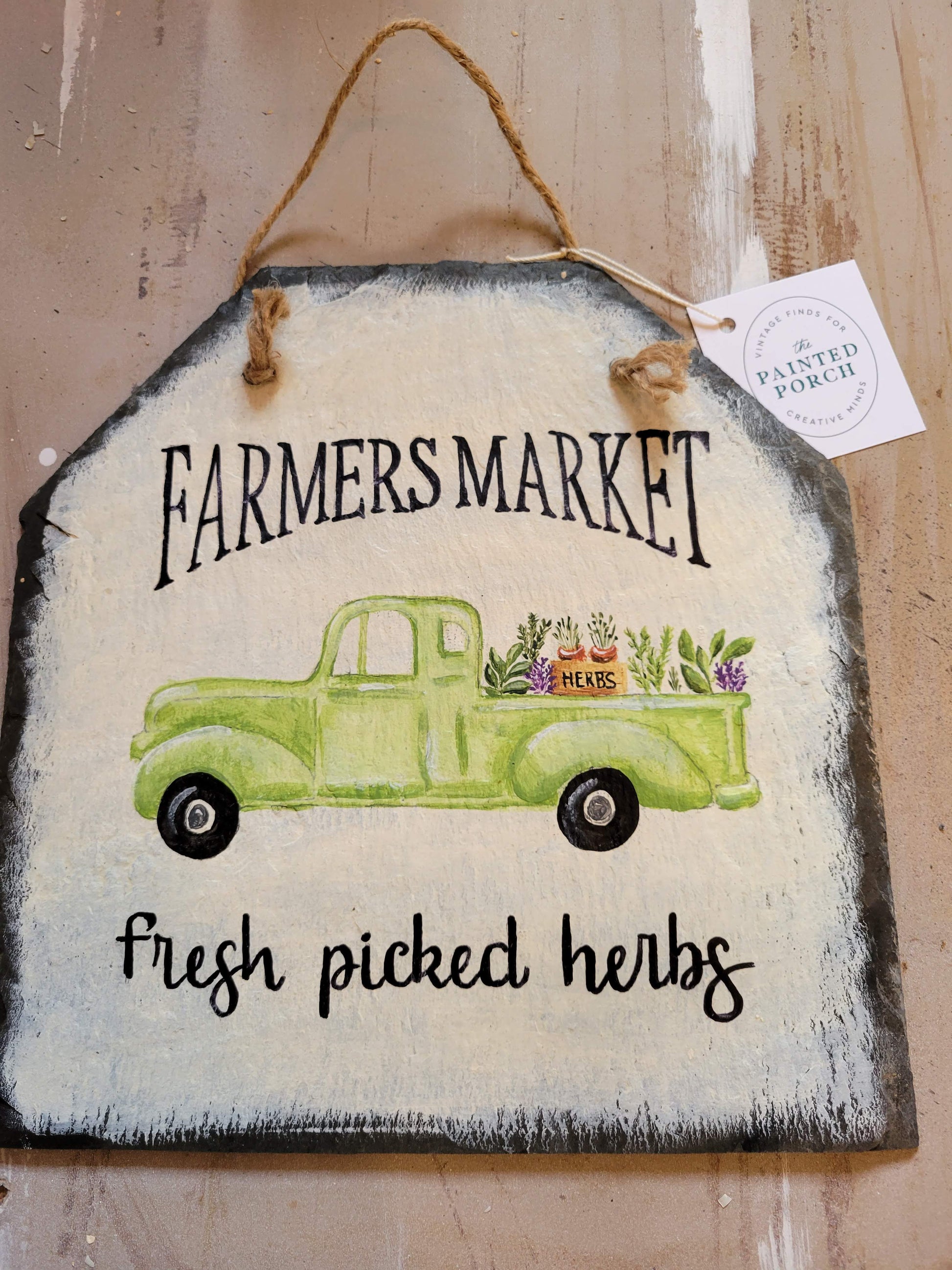 Natural slate sign painted white, with a hand painted green truck that is carrying plants. Handwritten "Farmers Market Fresh Picked Herbs," 11" x 11.5"