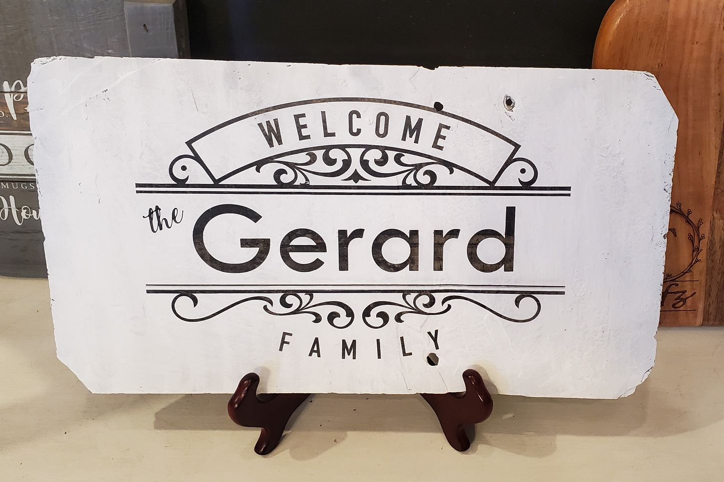 Welcome, The Gerard Family Slate Sign. The natural slate comes in a variety of sizes and this sample is approximately 10" x 16" wide. It will be painted white and personalized with your family name. This one does not have a hanger attached because it sits on an easel, but we can attach a jute rope hanger or a wire hanger if you wish to hang your sign.