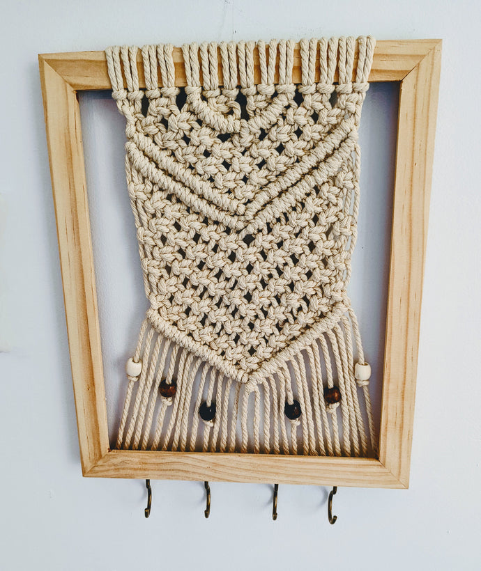 Macramé wall hanging on a neutral wood frame with wooden beads and hooks along the bottom to hold keys or something small.