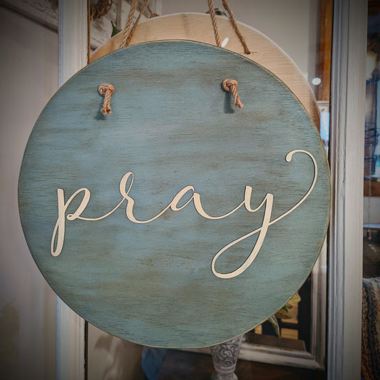 Round wooden sign painted teal with jute hanger and laser cut word "pray." Create this round sign door hanger! Paint or stain the wooden circle, paint your laser cut word, drill holes for the hanger. 
