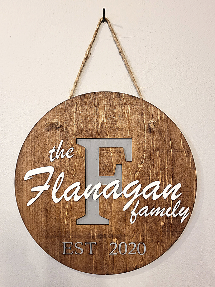 Personalized round wooden name sign. Customize with your family name and date established. Background of letter is painted light gray and laser cut name is painted white. Approximately 11