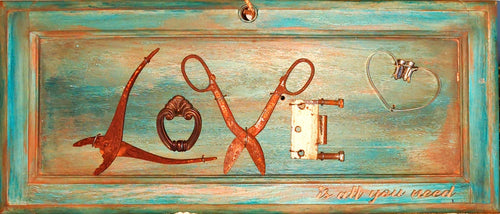 An upcycled cabinet door, painted and antiqued with wax, and a collection of found objects arranged to spell 