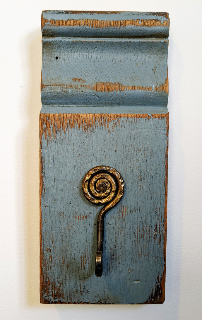 This gorgeous plinth was recovered from an old farm house. It has been painted blue and sanded. The interesting hammered metal spiral hook adds another dimension to this wall decor. 