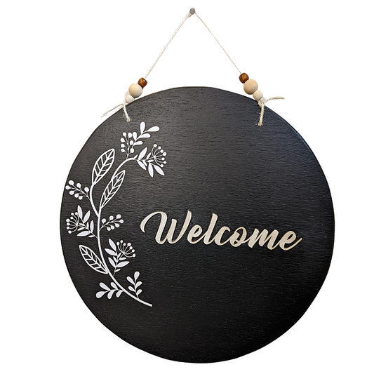 This black wooden Welcome sign has bohemian vibes with the three dimensional paper flower detail and multi-colored wooden beads. The "Welcome" is laser cut wood.