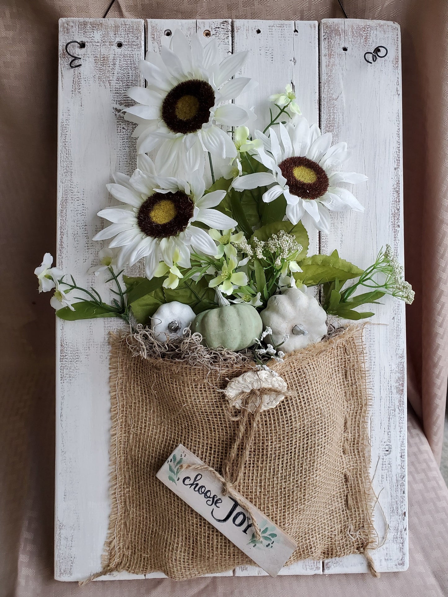 This rustic whitewashed pallet wood sign has a beautiful, neutral color scheme to fit most décor. The charming sunflower and pumpkin bouquet make it a great addition to your fall decoration collection. sunflower and pumpkin bouquet in a burlap sack, tiny Choose Joy sign on wood, jute rope, metal wire hanger, large size 13" x 21".